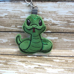 May include: Green plush snake keychain with a cute cartoon face and a red tongue. The snake is curled up in a relaxed pose.