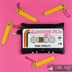 Könnte beinhalten: Schwarze Reißverschlusstasche mit einem weißen Kassettenband-Design. Das Kassettenband hat einen Regenbogenstreifen und den Text "Awesome 80s Mix" und "High Fidelity". Es gibt vier gelbe Bleistiftschlüsselanhänger mit rosa und grünen Akzenten.