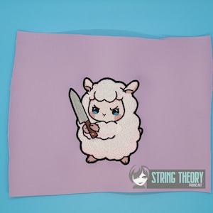 May include: Embroidered patch featuring a fluffy white sheep holding a knife, with blue eyes and a determined expression. The patch is on a lavender background, with the text "STRING THEORY FABRIC ART" in white.