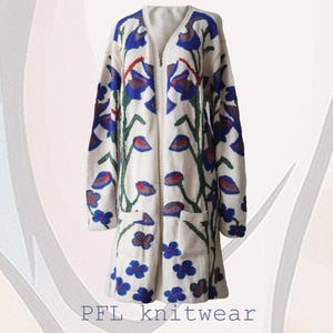 Puede incluir: Un cárdigan blanco con un patrón floral en tonos azules, verdes y rojos. El cárdigan tiene una cremallera y dos bolsillos. PFL knitwear.