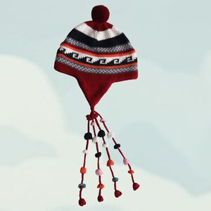 May include: A maroon knit hat featuring a white and black horizontal striped pattern, a wave motif, and a solid maroon pom-pom on top. The hat includes ear flaps with long, dangling braided cords adorned with small, multi-coloured pom-pom accents.