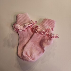 May include: A pair of pink ankle socks with a pink and white beaded trim.