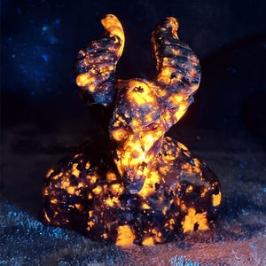 May include: A black and orange stone sculpture of a demon with horns. The sculpture is illuminated with a UV light, causing the stone to glow.