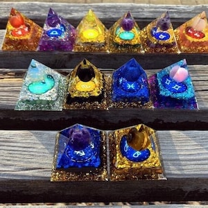 May include: A set of 12 crystal pyramids with gold accents and zodiac symbols. Each pyramid features a different zodiac sign and a crystal in a variety of colors, including blue, green, purple, and yellow.