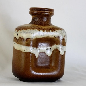 May include: A square-shaped ceramic vase with a narrow neck and a thick, raised rim. The body features a deep brown base glaze with a prominent, horizontal band of creamy white glaze that drips down the sides, creating a textured, layered effect.