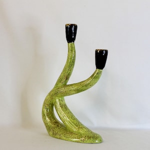 May include: A ceramic dual-arm candle holder featuring a textured, mottled lime green finish on the base and stems, transitioning into smooth, glossy black cups at the top of each arm. The structure has an asymmetrical, curved, and organic form.