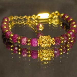 May include: A gold bracelet with a decorative charm and pink gemstone beads.