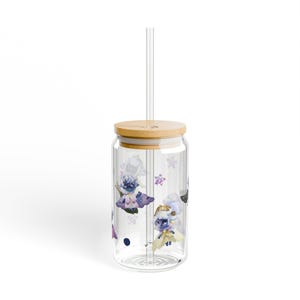 May include: A clear glass tumbler with a bamboo lid and a straw. The tumbler has a colorful cartoon design featuring characters with wings and stars.