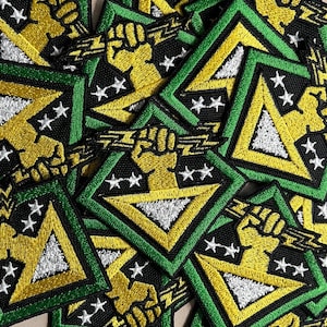 Puede incluir: Un conjunto de parches bordados con un diseño geométrico. Cada parche presenta un puño amarillo sosteniendo un rayo, un triángulo verde y amarillo, estrellas blancas y un fondo negro.
