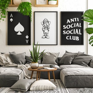 May include: A living room interior with a gray sectional sofa, three framed prints on the wall, and a small wooden coffee table. The prints feature a playing card, a cartoon character, and the text "Anti Social Social Club".