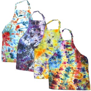 May include: Four aprons featuring tie-dye patterns in various color combinations. Each apron has an adjustable neck strap with a black plastic buckle and a front pocket. The patterns include blue, red, yellow, purple, and orange hues.