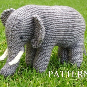 Peut inclure: Un jouet en forme d'éléphant en tricot gris avec des défenses en laine blanche. L'éléphant est debout sur de l'herbe verte.