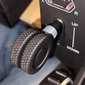 Może przedstawiać: Zbliżenie czarnego panelu sterowania samolotu z selektorem biegów. Panel zawiera słowo "GEAR" na podświetlanym białym i czerwonym wyświetlaczu. Widoczne jest teksturowane czarne pokrętło wraz z innymi etykietami sterowania.