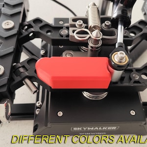 May include: Close-up of a black and silver mechanical device with a bright red component. The device has multiple metal parts, including springs, bolts, and what appears to be a control arm. The text "DIFFERENT COLORS AVAILABLE" is at the bottom.