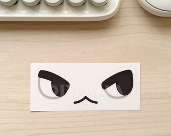 May include: A white sticker featuring a cartoon face with black, angry-looking eyes and a small, curved mouth. The word "MARSHAL" is printed in large, white capital letters below the sticker.
