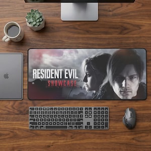 Pode incluir: Um mousepad retangular preto com o texto "RESIDENT EVIL SHOWCASE" e imagens de duas pessoas. Um teclado, um mouse, um tablet, uma xícara de café e uma planta suculenta estão visíveis em uma mesa de madeira.