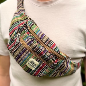 Pode incluir: Cinto de cintura listrado multicolorido com três compartimentos com zíper e um zíper marrom. A bolsa tem uma etiqueta que diz "EVEREST GEAR". A bolsa é feita de tecido tecido com uma variedade de cores, incluindo vermelho, verde, roxo e marrom.