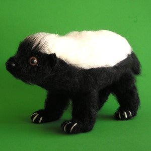 Puede incluir: Un juguete de peluche de tejón de miel negro y blanco con una franja blanca en la espalda. El juguete tiene una nariz negra, ojos marrones y garras blancas.