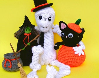 May include: A crocheted Halloween scene featuring a white ghost, a witch with a green hat and a black cat wearing a pumpkin costume.