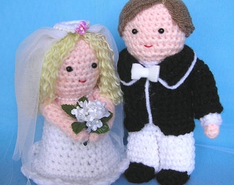 May include: A crocheted bride and groom doll set. The bride is wearing a white dress with a veil and holding a bouquet of white flowers. The groom is wearing a black suit with a white bow tie.