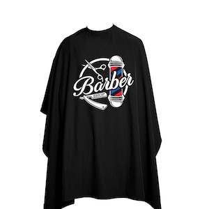 Puede incluir: Capa de barbero negra con un logotipo blanco que presenta una barra de barbero, tijeras y una navaja con el texto "Barber Shop".