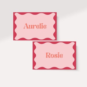 May include: Two pink place cards with scalloped edges and red borders. The top card says "Aurelie" and the bottom card says "Rosie".