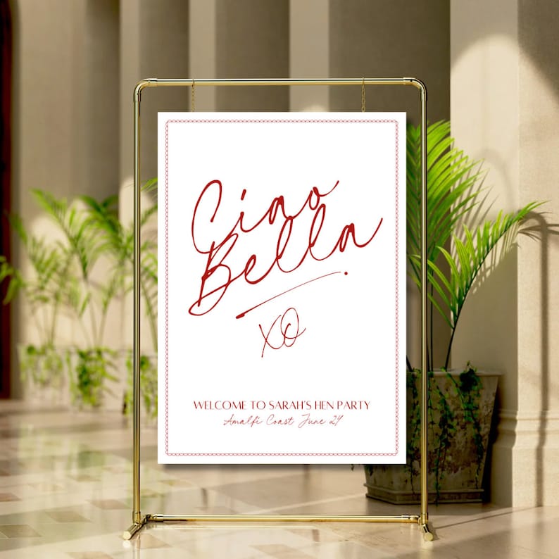 May include: A white sign with a gold frame, featuring the text "Ciao Bella" in red cursive script, followed by "XO" in red. Below the text, it reads "Welcome to Sarah's Hen Party Amalfi Coast June 21st".