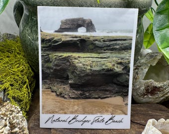 May include: A photograph of Natural Bridges State Beach, featuring a natural rock arch in the ocean. The image shows the rugged coastline with waves crashing against the rocks. The text "Natural Bridges State Beach" is written in cursive at the bottom.
