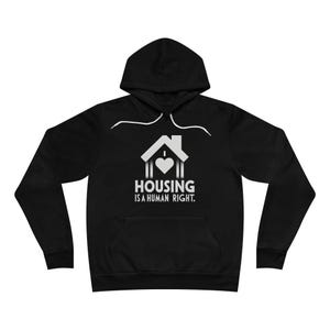 Könnte beinhalten: Schwarzer Kapuzenpullover mit weißer Grafik eines Hauses, Herzens und dem Text "HOUSING IS A HUMAN RIGHT." Der Pullover hat eine Vordertasche und einen weißen Kordelzug.