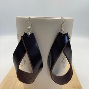 May include: A pair of brown leather earrings with a twisted design. The earrings are hanging from silver hooks.