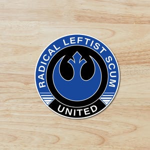 May include: A round sticker with a blue and black design. The text "RADICAL LEFTIST SCUM" is in a blue ring around the edge. The word "UNITED" is at the bottom. The sticker is on a wood grain surface.