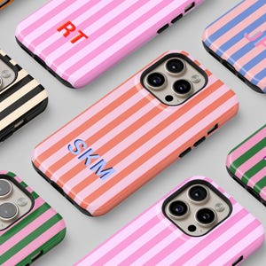 May include: A collection of colorful phone cases with striped patterns. Cases feature various color combinations, including pink, orange, blue, green, and black, with initials in the center. The cases are designed for a smartphone.