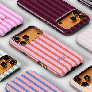 May include: A collection of colorful phone cases with striped patterns. Each case features a different color scheme, including pink, blue, green, and red stripes. Some cases have initials printed on them. The cases are designed to fit a smartphone.