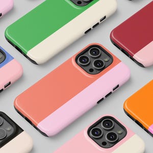 Puede incluir: Surtido de fundas de teléfono coloridas con un diseño de dos tonos. Cada funda presenta una combinación de colores diferente con una franja contrastante en el medio. Las fundas están dispuestas en una cuadrícula.