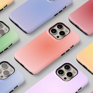 Puede incluir: Una variedad de fundas de teléfono de colores pastel, incluyendo rosa, amarillo, verde y azul. Cada funda tiene un acabado brillante y un borde negro, resaltando el módulo de la cámara. Las fundas están dispuestas en un patrón de cuadrícula.