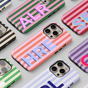 May include: A collection of phone cases with a striped design in various colors, including red, pink, green, and purple. Each case features a different set of three-letter initials in a contrasting color. The cases are arranged on a light gray surface.