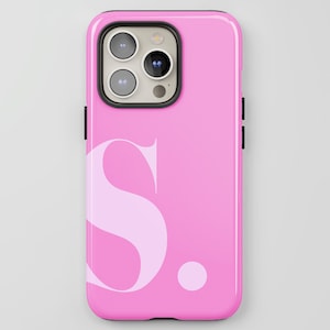 以下が含まれることがあります： 大きな薄いピンク色の文字「S」と小さなドットが付いたピンク色の携帯電話ケース。ケースは光沢仕上げで、カメラと側面に黒い縁取りがあります。携帯電話ケースはスマートフォン向けに設計されています。