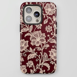 May include: A smartphone case featuring a deep burgundy background with a repeating cream-colored floral lace pattern. The design includes intricate blossoms, leaves, and vines that cover the entire surface of the protective phone cover.