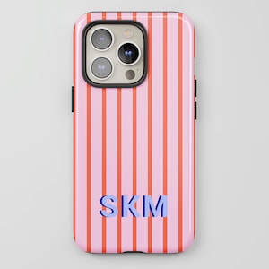 May include: Pink phone case with vertical orange stripes. The case features the initials "SKM" in blue. The phone case has a glossy finish and a black border around the camera.