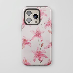 Könnte beinhalten: Eine rosa und weiße Handyhülle mit einem Blumendesign mit rosa Lilien. Die Hülle hat einen schwarzen Kameraausschnitt und einen schwarzen Rand.