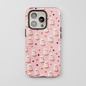 May include: A pink phone case featuring a pattern of white ghosts and orange stars. The case is designed for a phone with a camera bump.