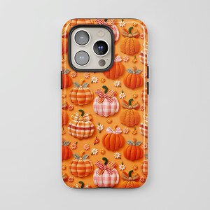 Puede incluir: Funda de teléfono con un patrón repetido de calabazas naranjas con lazos de tela y pequeñas flores blancas sobre un fondo naranja. La funda tiene un borde negro y un recorte para la cámara.