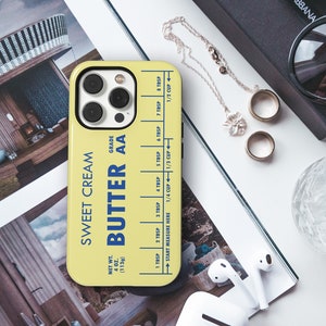 May include: A yellow phone case with a blue and white design that says "Sweet Cream Butter AA" and has a measurement guide for tablespoons and cups. The case is for an iPhone.