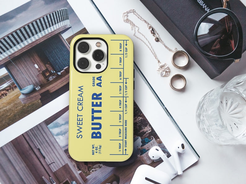 May include: A yellow phone case with a blue and white design that says "Sweet Cream Butter AA" and has a measurement guide for tablespoons and cups. The case is for an iPhone.