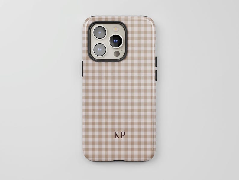 Puede incluir: Una funda para smartphone con un patr&oacute;n de cuadros vichy en color beige claro y blanco. La funda tiene un recorte para un sistema de triple c&aacute;mara y las letras KP est&aacute;n impresas en una fuente serif marr&oacute;n oscuro en la parte inferior.