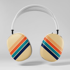 May include: White over-ear headphones with cream-colored earcups. Each earcup features diagonal stripes in orange, teal, and navy blue. The headband is white, and the design has a retro aesthetic.