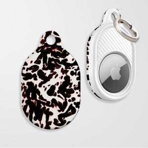 May include: Two AirTag accessories. One is a tag with a black and white pattern, the other is a white AirTag holder with a silver key ring. The AirTag has a silver Apple logo.