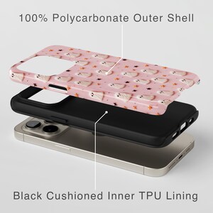 May include: A pink phone case with a ghost pattern and the text "100% Polycarbonate Outer Shell". The case is shown with a black cushioned inner TPU lining and a gold phone.