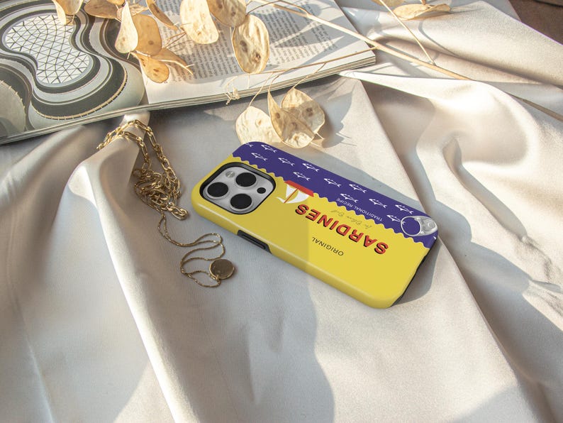 May include: A yellow phone case with a blue and white sardine can design. The can says "ORIGINAL" and "SARDINES" in a retro font. The case has a cutout for the phone camera.