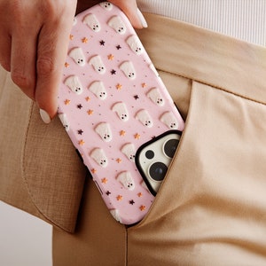 May include: A pink phone case with a pattern of white ghosts and orange stars. The case is in someone's pocket.